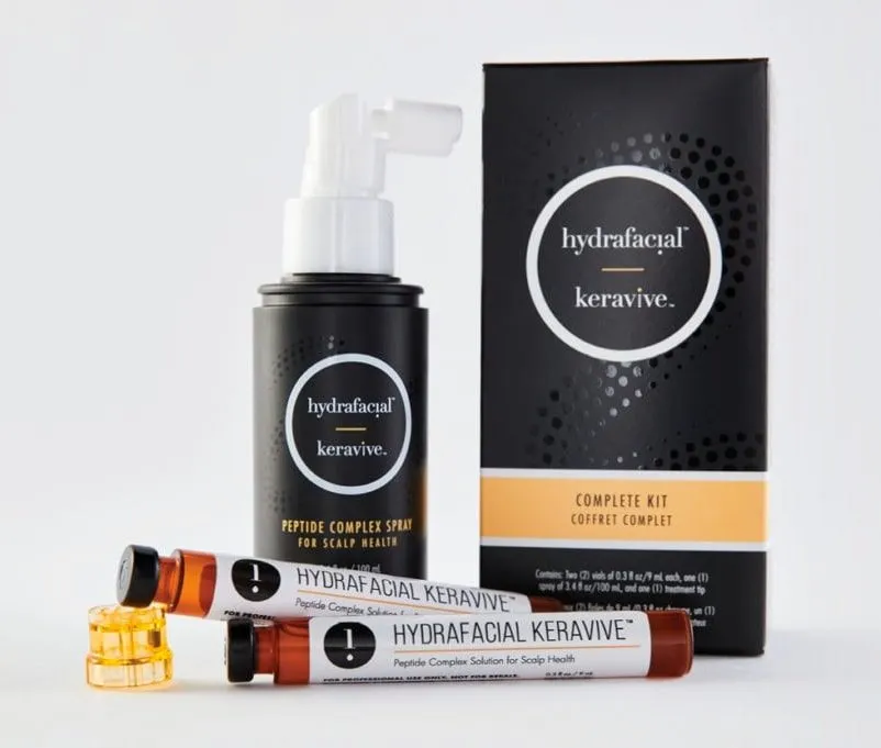 hydrafacial product 2 A Hydrafacial Keravive Complete Kit, featuring a black spray bottle, two small vials labeled Keravive, a black box with branding, and two yellow capsules, arranged on a white surface.